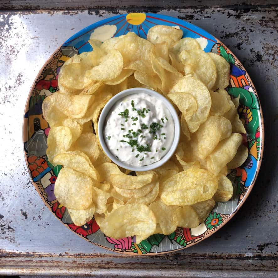 Homemade Hiland French onion dip copycat recipe in a ceramic dish surrounded by ridged potato chips, showing the creamy all-natural dip ready to serve. A nostalgic meatless lenten snack or appetizer.
