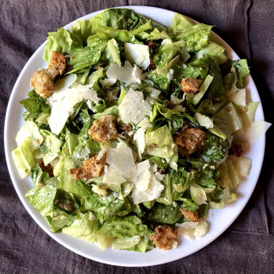 Homemade Caesar salad on a serving platter with shaved Parmigiano-Reggiano cheese, super crispy homemade Parmesan herbed croutons, and scratch-made Caesar dressing with anchovies. A classic lenten salad perfect for topping with grilled shrimp.