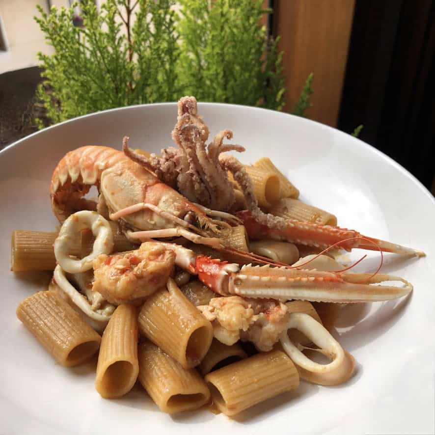 Italian langoustine scampi and squid tossed with rigatoni pasta in a light garlic white wine sauce, showing whole langoustines and tender squid rings over ridged rigatoni. An impressive lenten Italian seafood pasta.