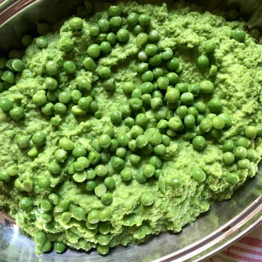 A serving platter filled with smooth creamy mushy peas garnished with whole peas on top, showing the vibrant green color and velvety texture. A classic British side dish perfect alongside lenten fish and chips.