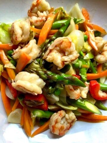 Shrimp and vegetable stir fry in a light Cantonese white sauce with sauteed shrimp, carrots, asparagus spears, cabbage, and peas in a serving bowl. An easy and healthy lenten Asian seafood dinner.