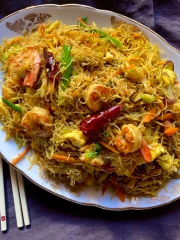 Homemade Singapore noodles on an oval platter with chopsticks showing how to make shrimp mei fun at home.