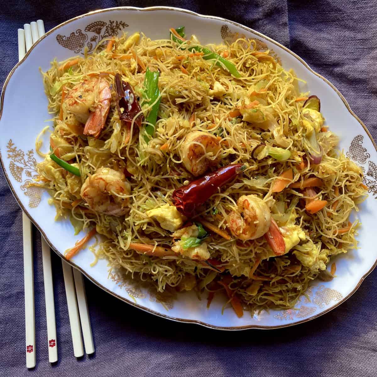 Homemade Singapore noodles on an oval platter with chopsticks showing how to make shrimp mei fun at home.