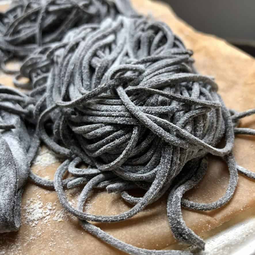 Cuttlefish spaghetti alla chitarra al nero di seppia nests dusted with flour on tray ready to cook or freeze, fresh squid ink noodles for nero di seppia pasta.