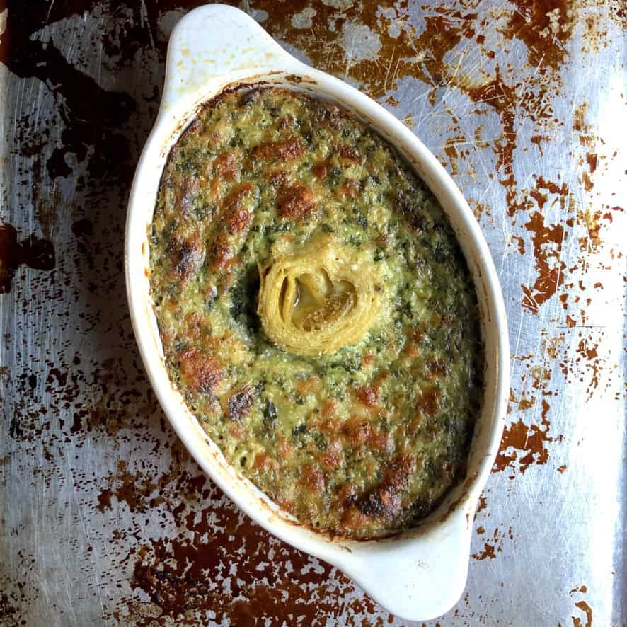 Homemade spinach artichoke dip in a traditional oval gratin dish, golden brown and bubbly with a whole artichoke heart in the center. A crowd-pleasing meatless lenten appetizer or snack.