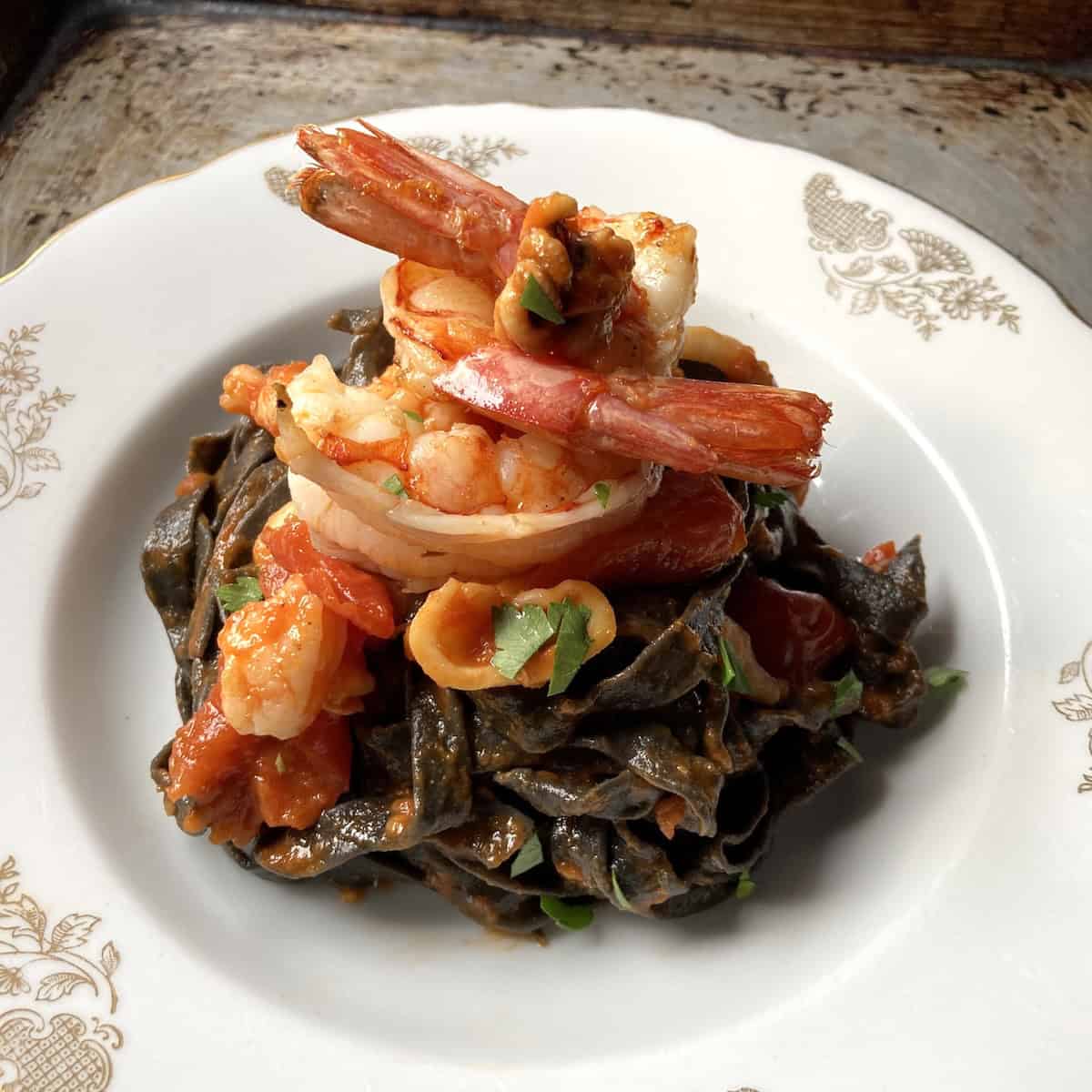 Squid ink fettuccine with red Argentinian shrimp, Italian shrimp, and cuttlefish in white wine garlic tomato sauce, homemade black pasta with seafood.