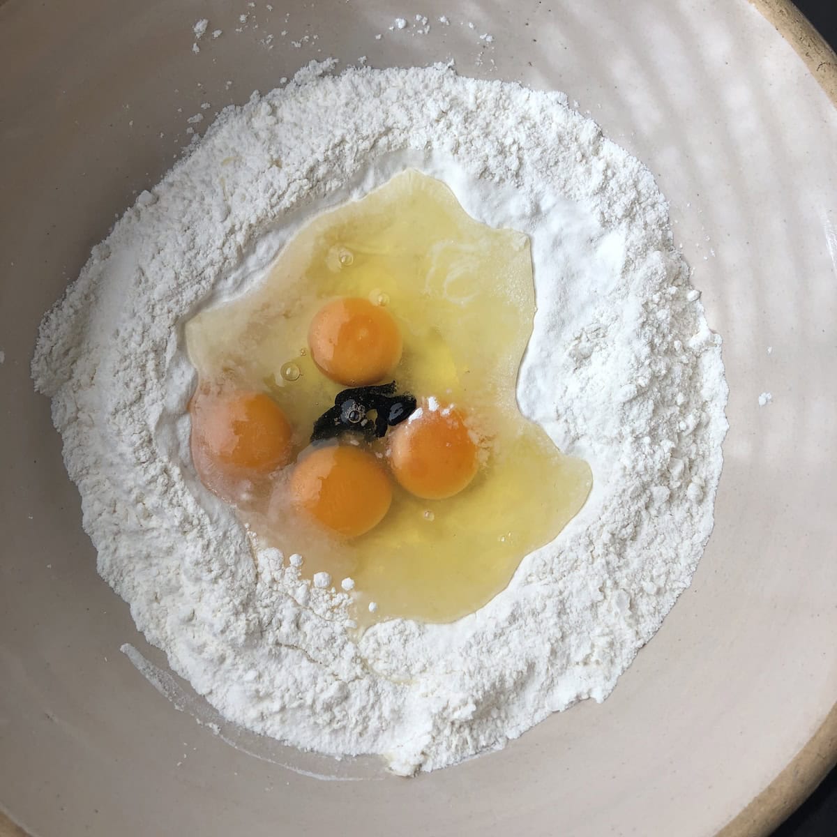 00 flour with 4 eggs cracked into the well and squid ink added to make black pasta dough, how to make squid ink pasta showing cuttlefish ink mixed with eggs for this homemade nero di seppia pasta recipe.
