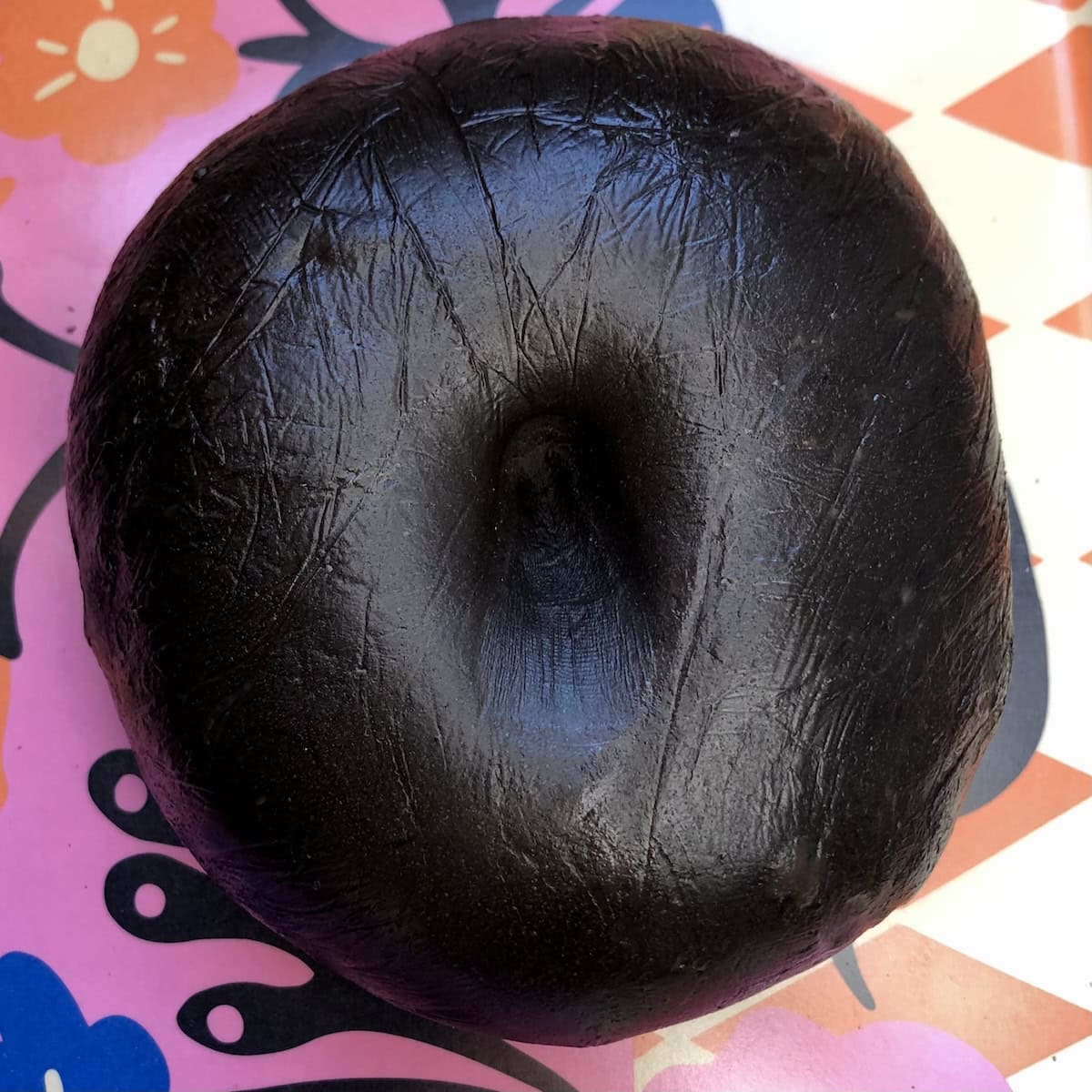 Shiny black pasta dough ball with my finger indentation in the middle after resting, ready to portion and roll for fresh squid ink pasta.
