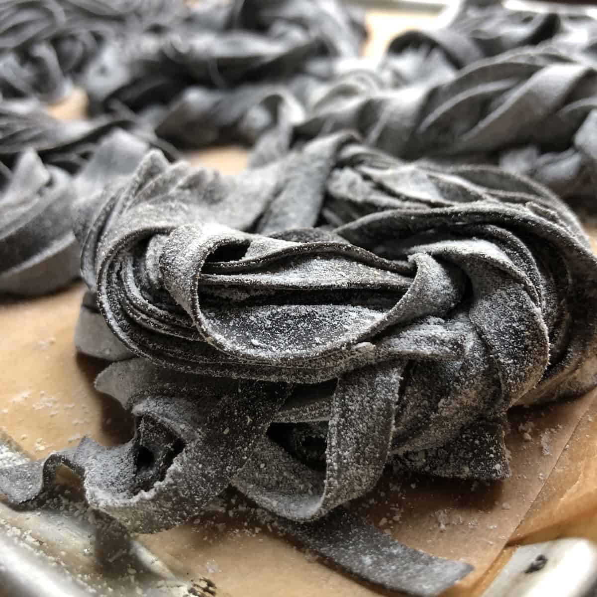 Fresh homemade squid ink pasta nests on a board showing the jet black color of this nero di seppia pasta recipe, how to make squid ink pasta from scratch for halloween dinner ideas or seafood pasta dishes.
