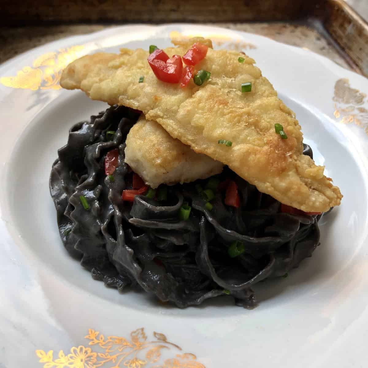 Black squid ink tagliatelle with creamy alfredo sauce and pan-fried cod filet, homemade nero di seppia pasta with white sauce and fish.
