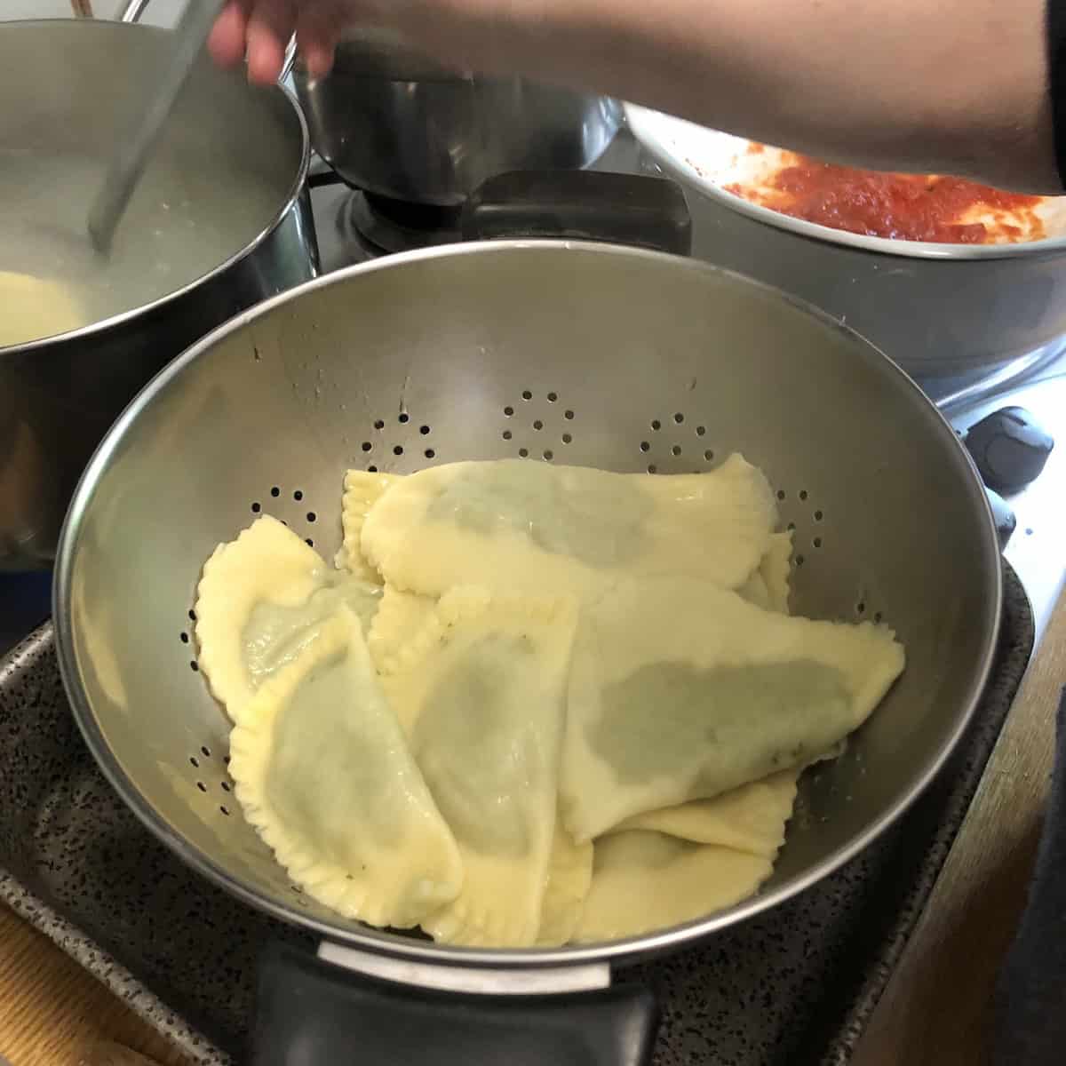 Al dente 00 flour spinach and ricotta ravioli strained in a colander after floating to the top of the water - how to tell when ravioli is done and ready to be added to sauce.