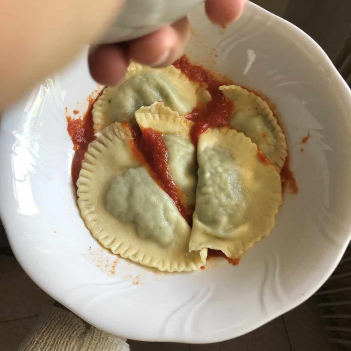 Cooked and drained 00 flour spinach and ricotta ravioli added to a serving dish with tomato sauce - the traditional Italian method for what sauce to serve with spinach ravioli.