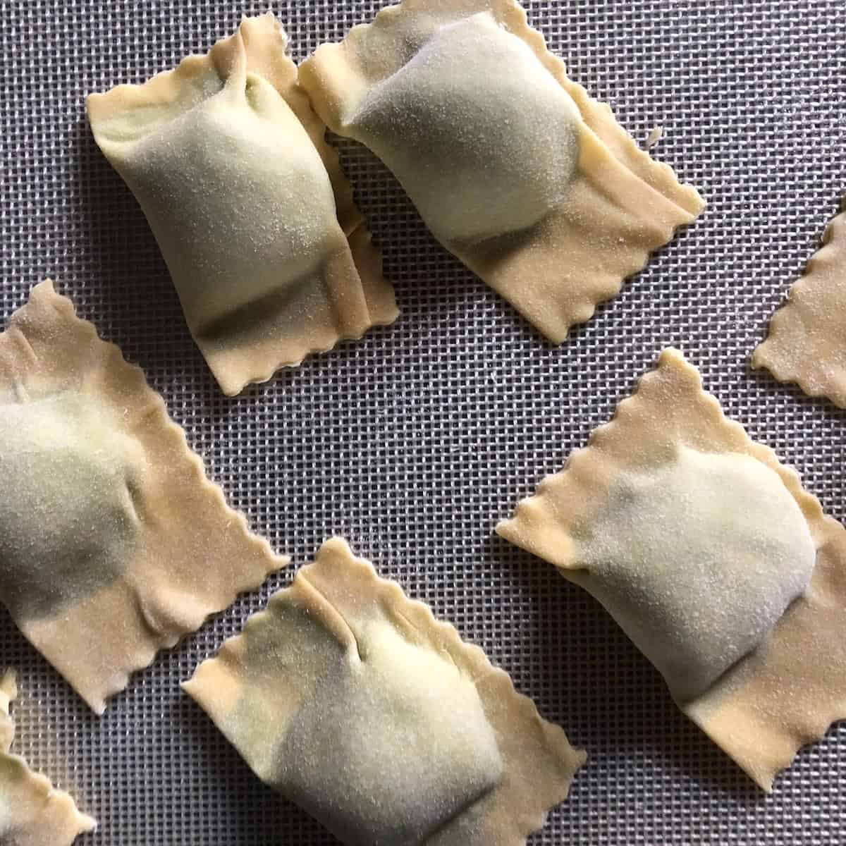 Uncooked square 00 flour spinach and ricotta ravioli made using an easy beginner folding technique - a simple starting point for how to make spinach and ricotta ravioli from scratch.