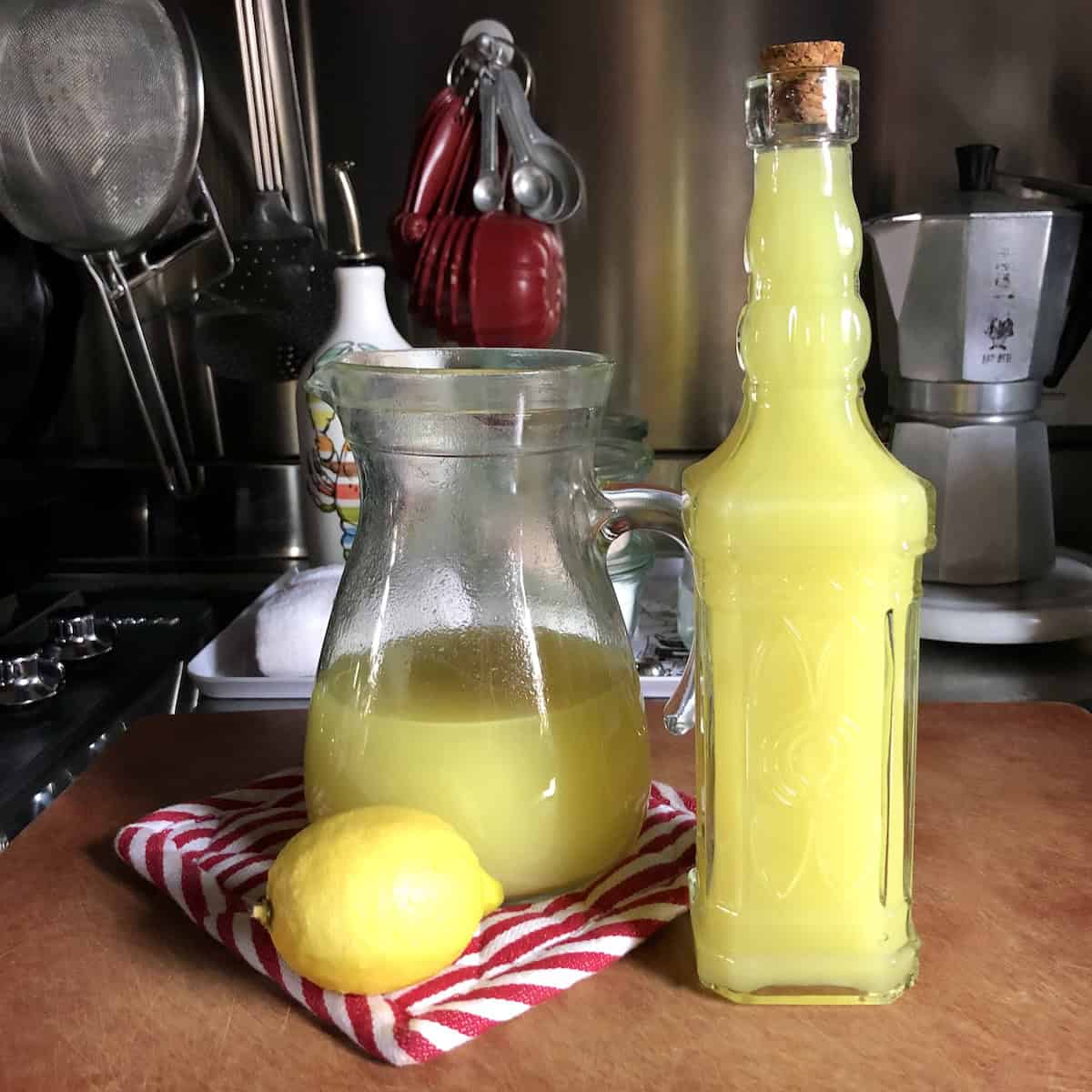 Homemade authentic Italian limoncello in decorative glass bottle with cork top next to pitcher of fresh limoncello and lemons, best mother's day brunch menu idea for limoncello spritz cocktail.