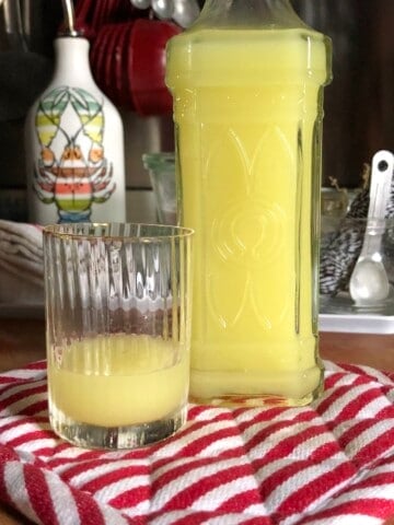 Homemade authentic Italian limoncello in decorative glass bottle with cork top next to pitcher of fresh limoncello and lemons, best mother's day brunch menu idea.