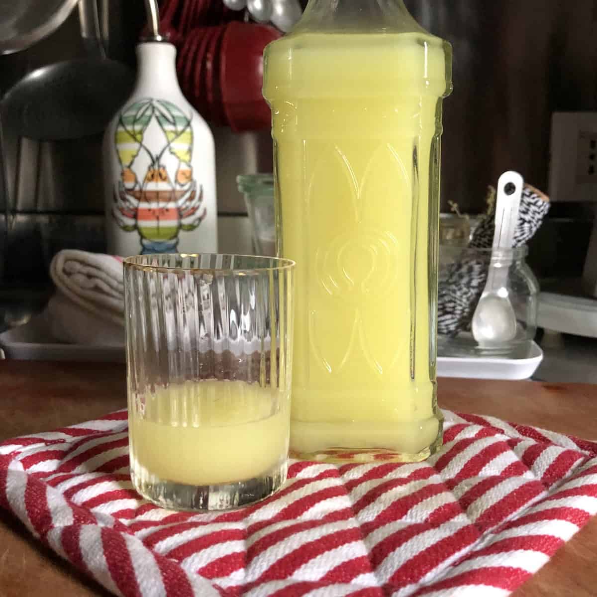 Homemade authentic Italian limoncello in decorative glass bottle with cork top next to pitcher of fresh limoncello and lemons, best mother's day brunch menu idea.