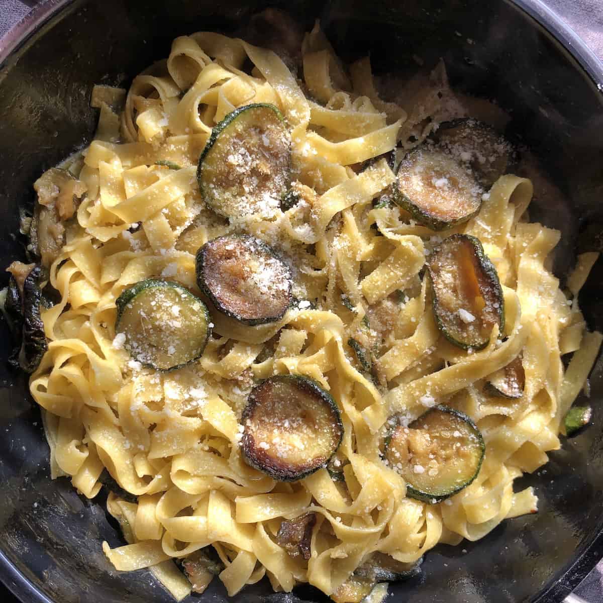 A skillet full of homemade pasta alle zucchine (or better known as pasta with zucchini with tagliatelle standing in for spaghetti and sprinkled with a handful of freshly grated aged Grana Padano cheese.