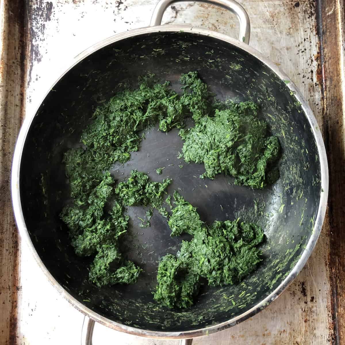 A skillet of chopped sautéed spinach with all moisture removed, ready to be added to the cheese mixture for an Italian spinach and ricotta ravioli filling.