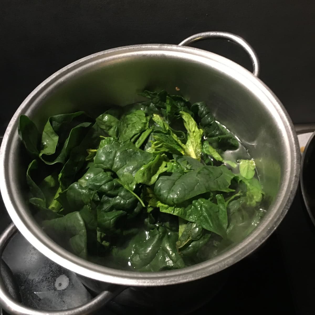 Fresh spinach leaves blanching in water showing the fresh spinach versus frozen spinach process for making spinach and ricotta ravioli filling.