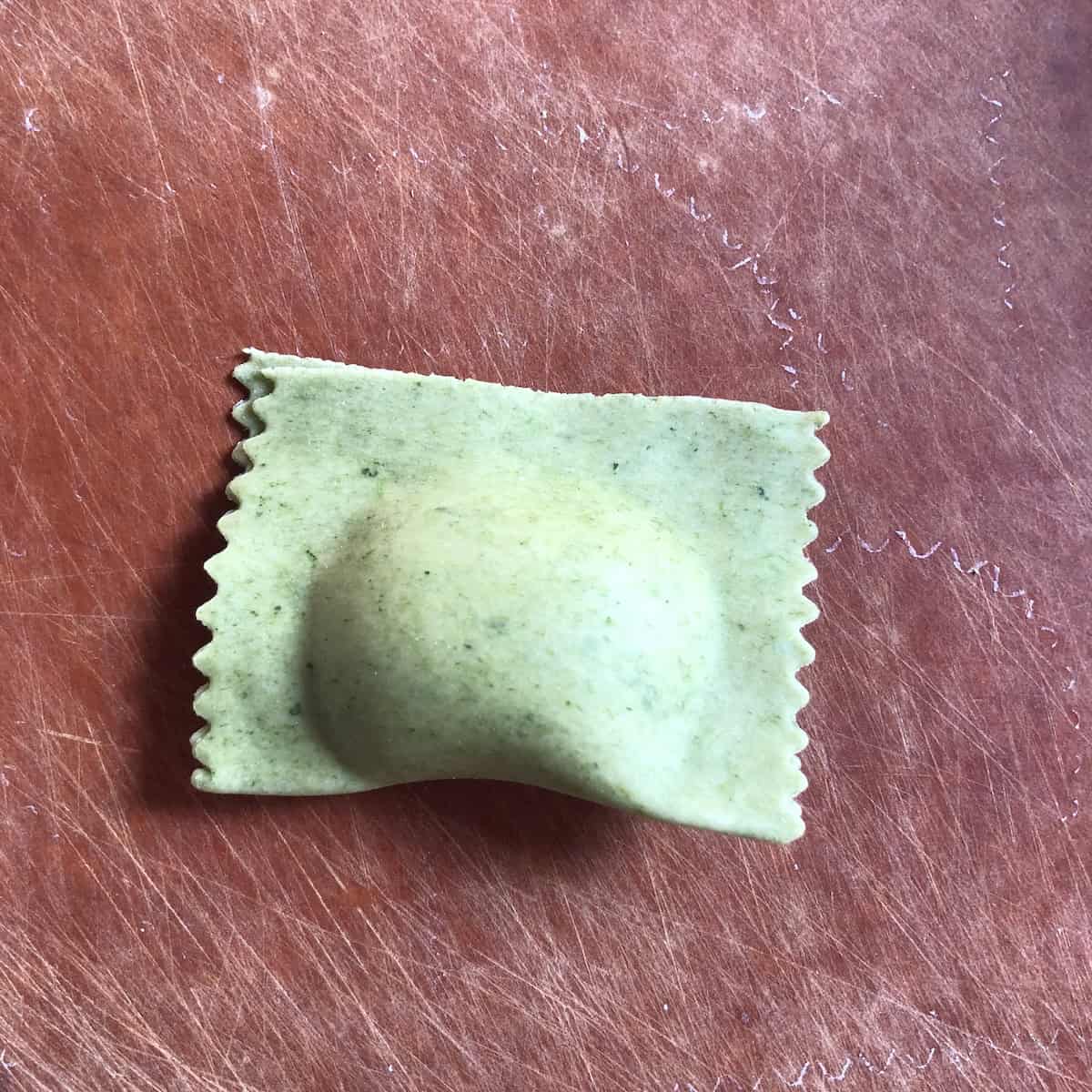 Green spinach pasta dough folded over the spinach and ricotta filling just before being cut into half moon crescent shaped mezzaluna ravioli.