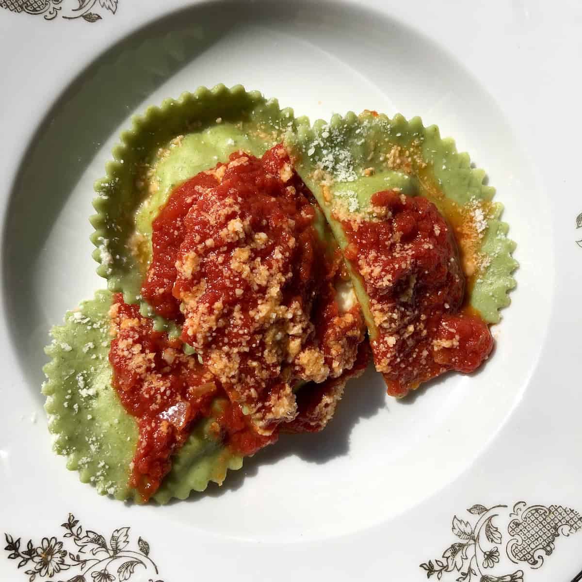 Three green mezzaluna spinach ravioli served in a pasta bowl with tomato sauce, ready to eat.