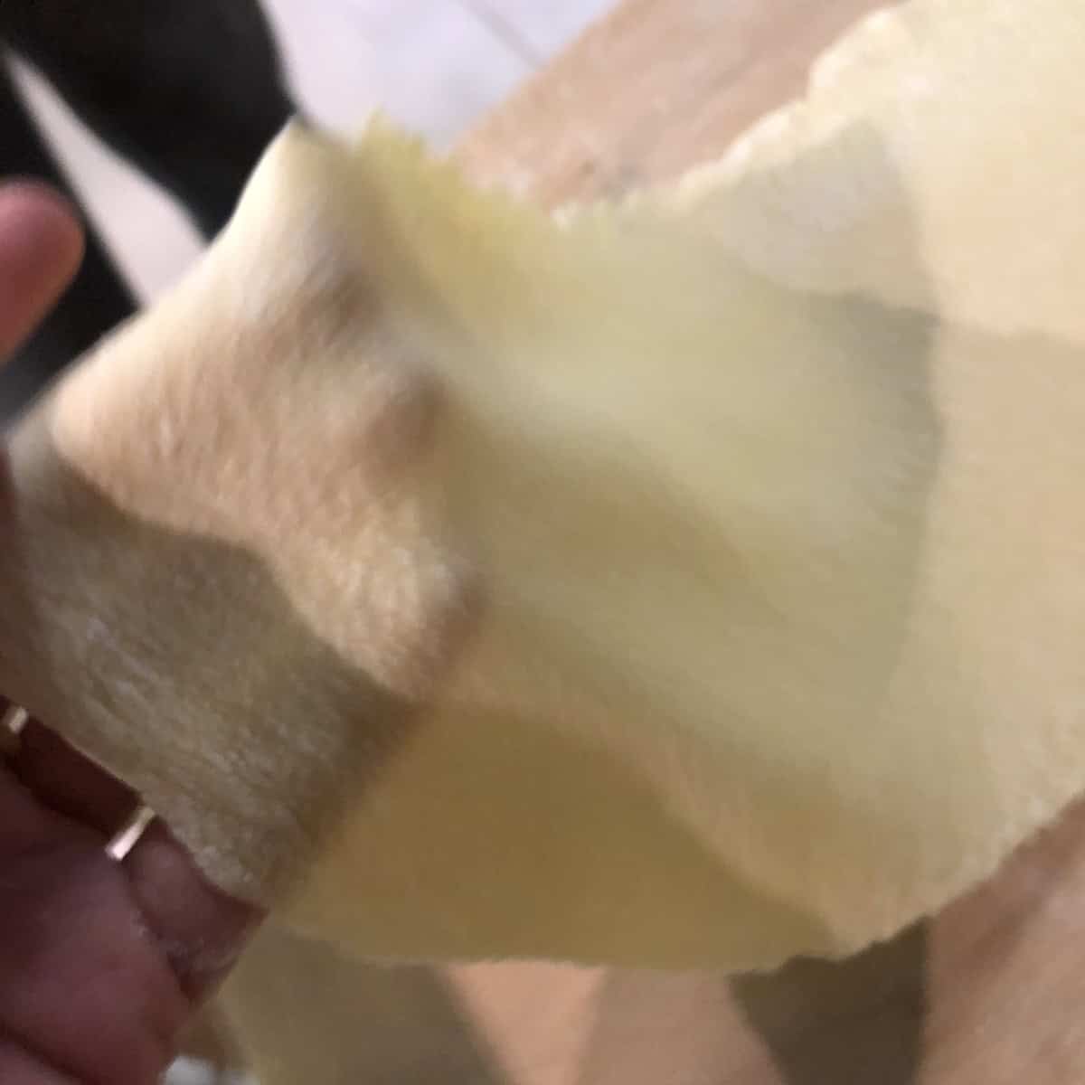 My hand holding up a thin sheet of Anna and my fresh pasta dough to show the correct thickness for how to make spinach and ricotta ravioli from scratch with the best texture.