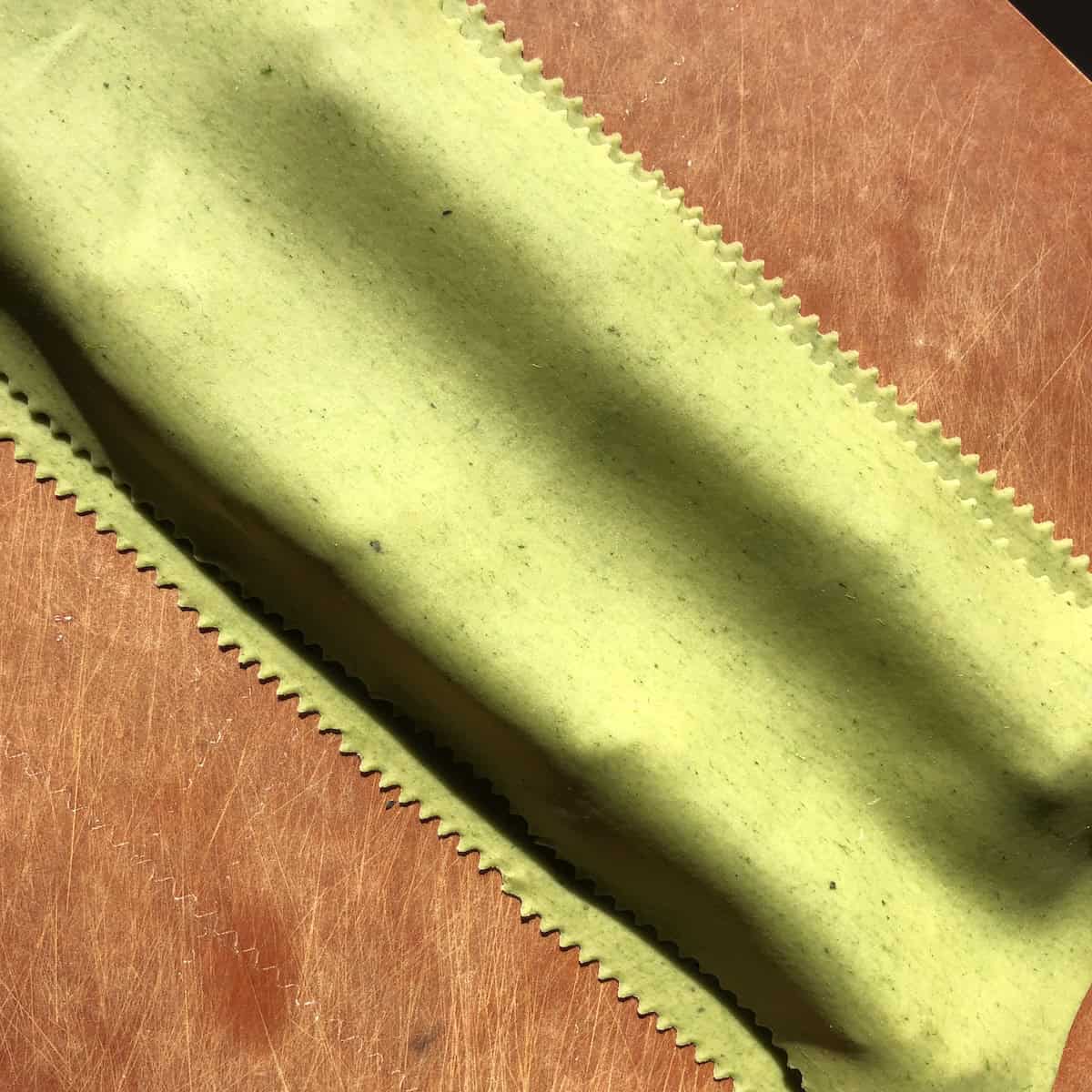 A fresh pasta sheet laid over mounds of spinach and ricotta filling, ready to be pressed to remove air bubbles and sealed to make homemade spinach and ricotta ravioli.