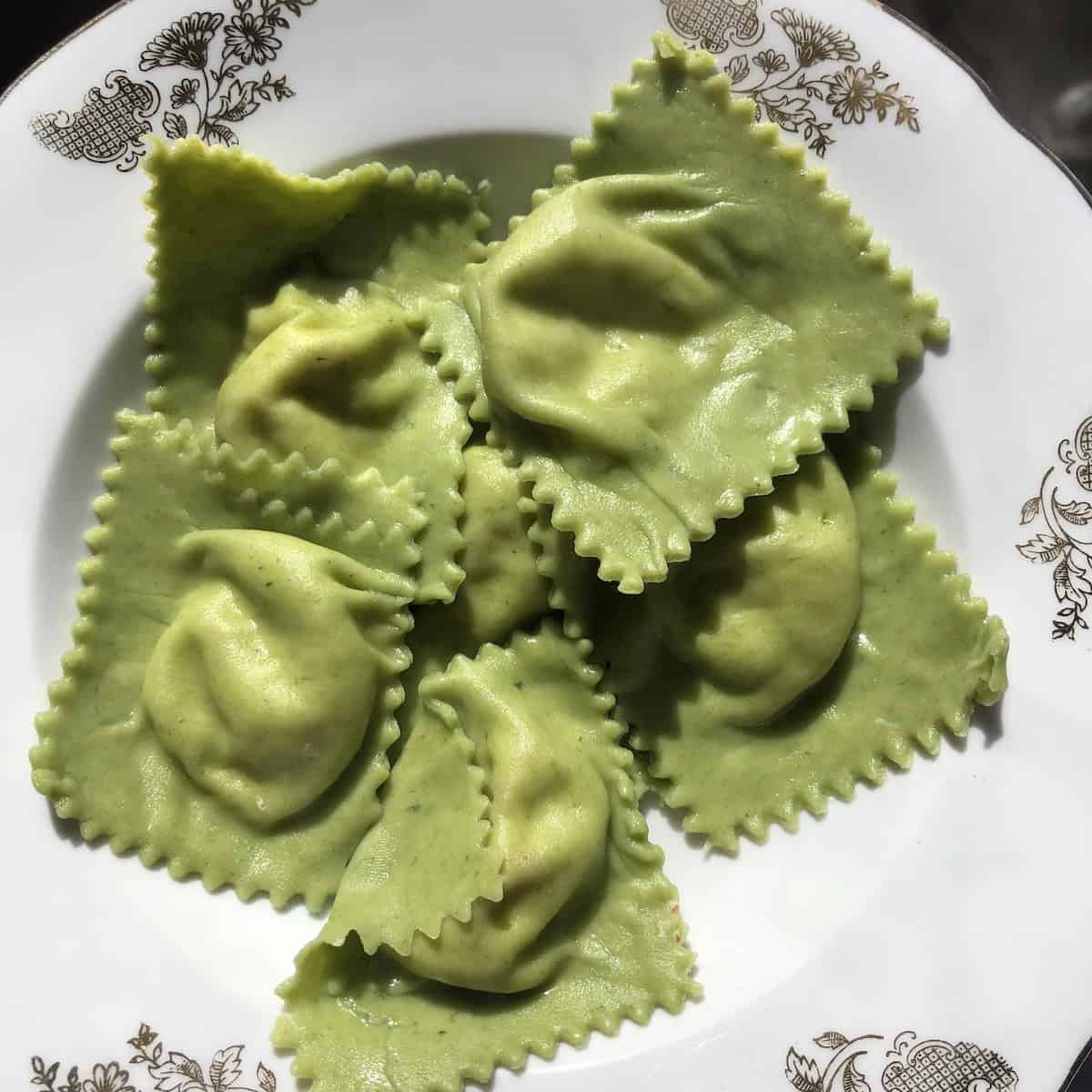 Freshly cooked green spinach and ricotta ravioli strained on a plate, ready to be added to a serving platter and finished with sauce - knowing how do you know when ravioli is cooked makes all the difference.