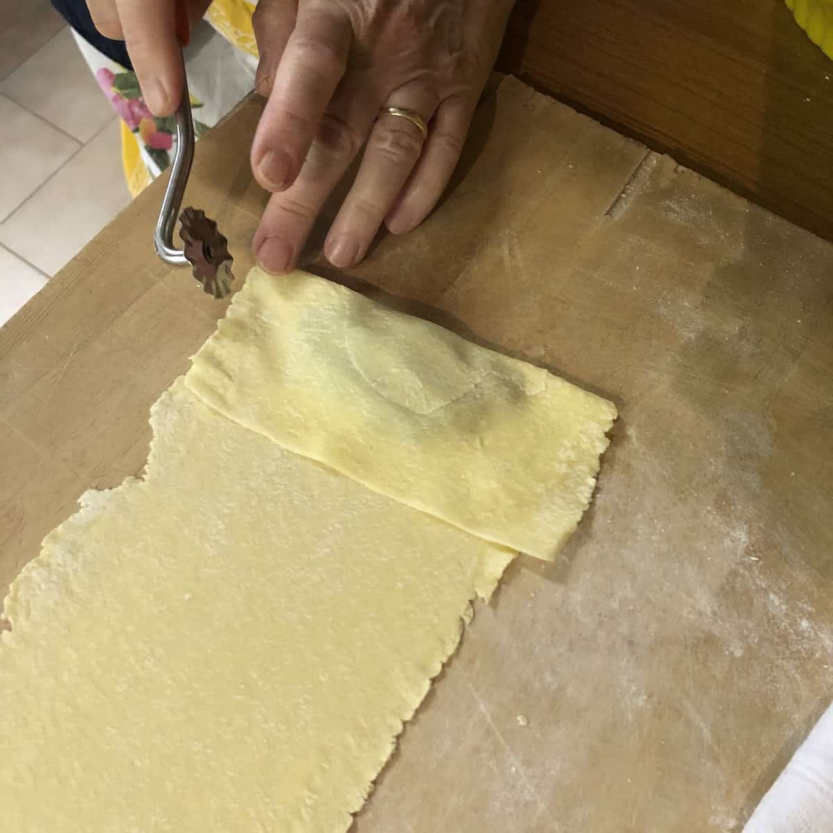 Nonna Anna cutting freshly folded mezzaluna spinach and ricotta ravioli using a wavy pastry wheel cutter, the traditional Italian ravioli recipe method passed down through generations.