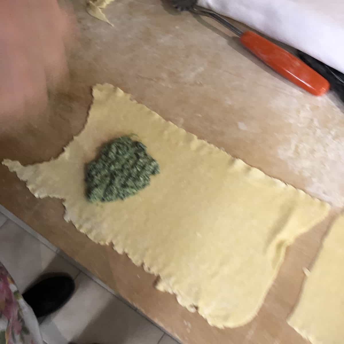 he perfect amount of spinach and ricotta filling portioned onto a fresh pasta sheet for traditional Easter mezzaluna ravioli - the key to a well-balanced traditional ravioli filling.