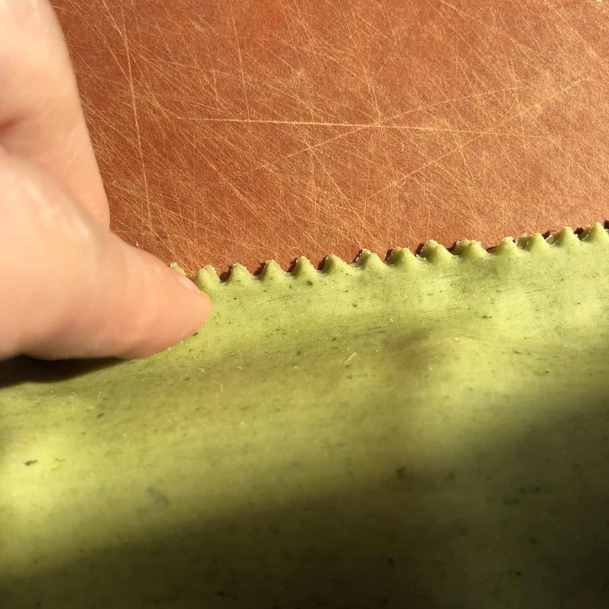 Pressing down on green spinach pasta dough over the spinach and ricotta filling to line up the edges before pressing out all the air and sealing the ravioli.