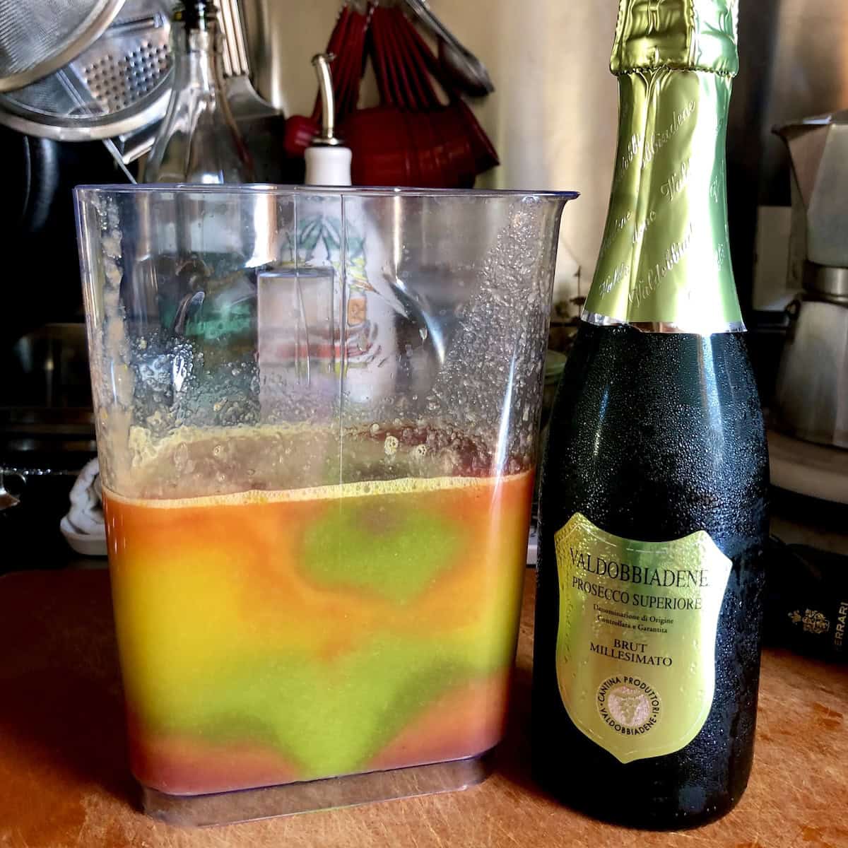 Pitcher of tie-dyed rainbow fresh pressed juice from pineapples, blueberries, strawberries, blood oranges, and kiwi next to chilled prosecco for brunch bellini cocktails, mother's day brunch ideas.