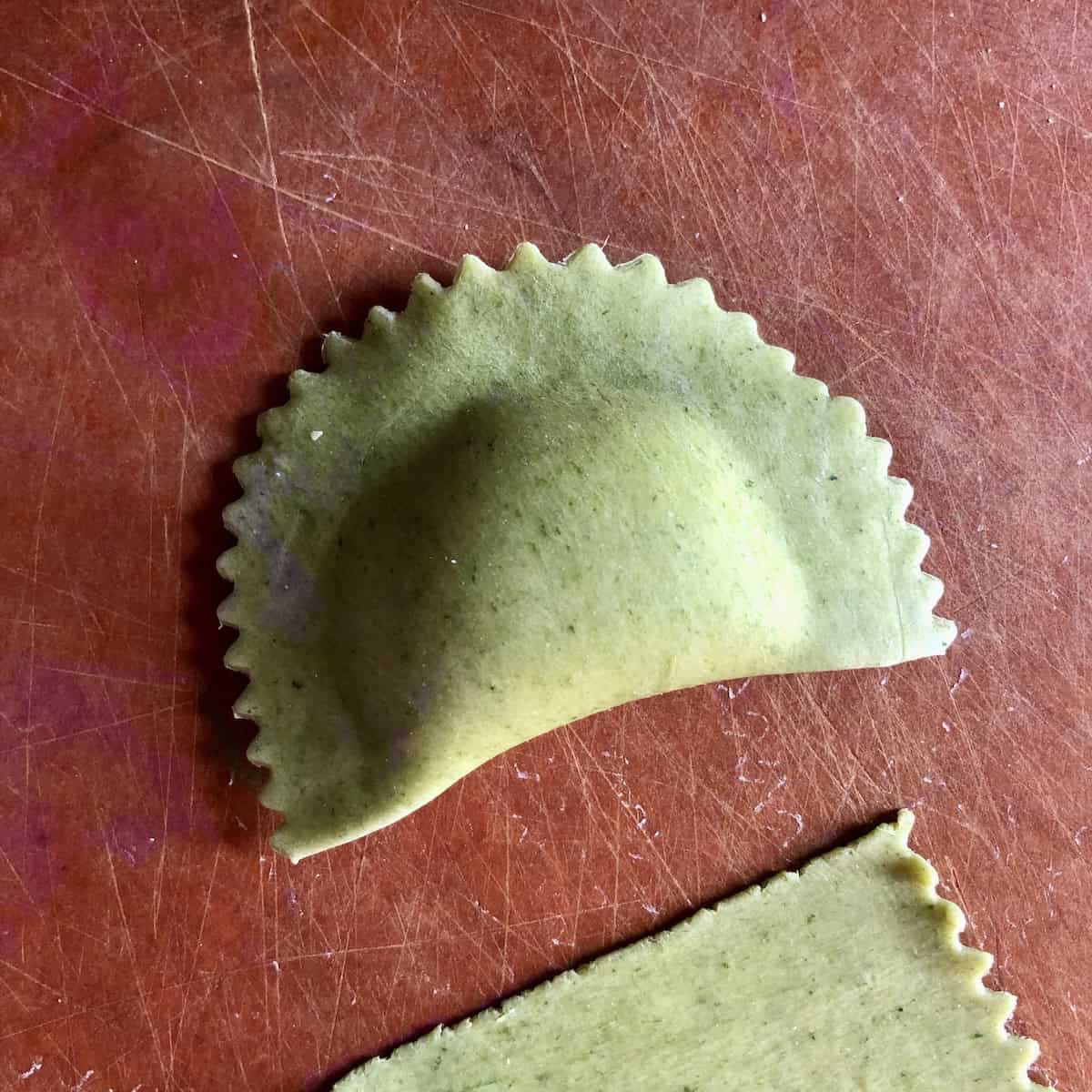A fully sealed green spinach pasta mezzaluna shaped spinach and ricotta ravioli on a cutting board with all air removed and edges pressed tight.