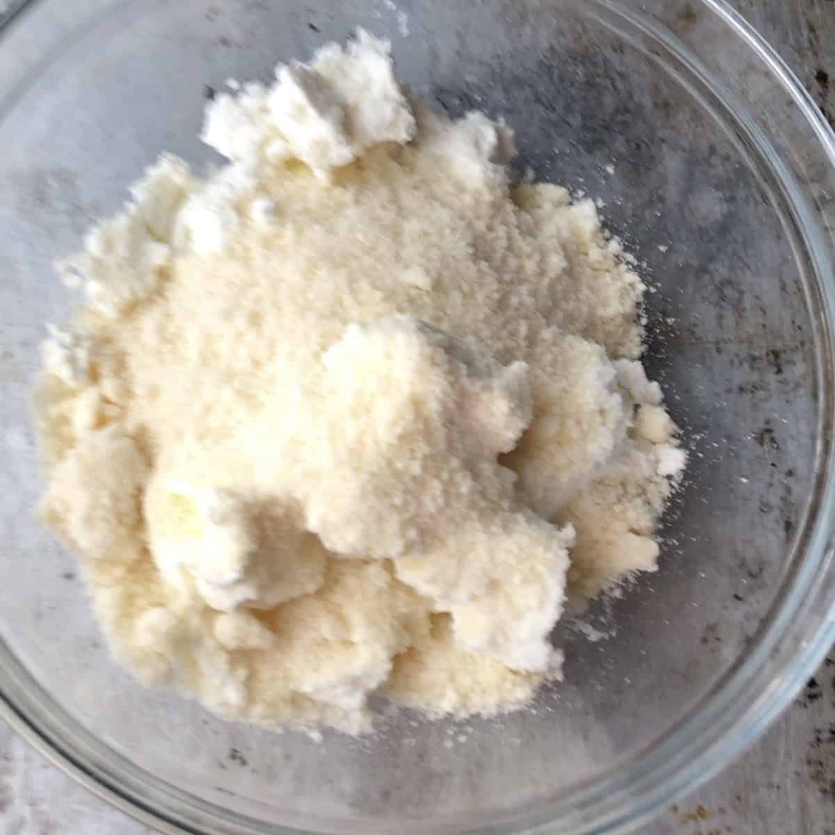 Strained ricotta, Grana Padano, mascarpone, salt, black pepper, and freshly grated nutmeg combined in a mixing bowl ready to stir together for a spinach and ricotta ravioli filling.