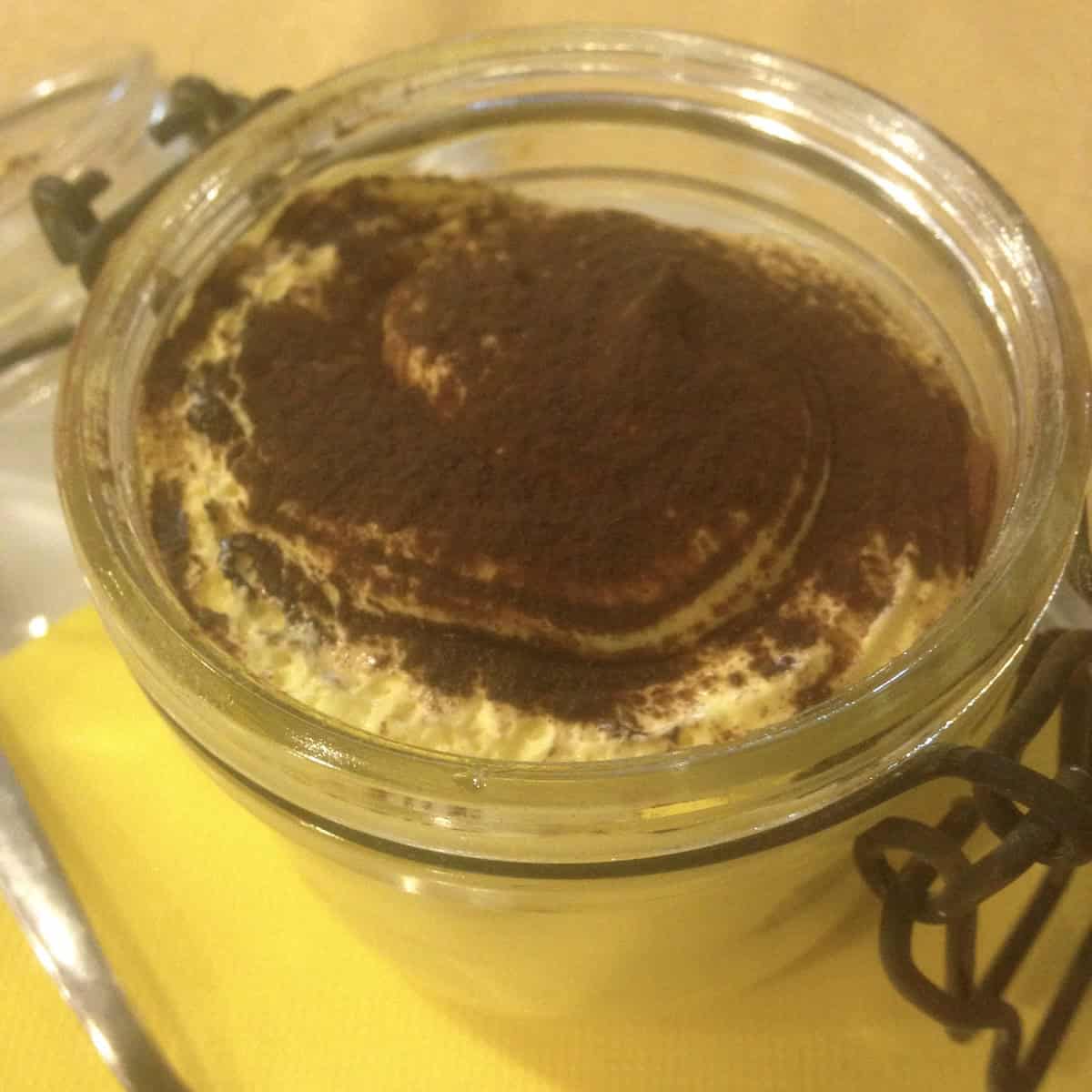Restaurant tiramisu layered in a hermetic glass canning jar with a ladyfinger on top dusted with cocoa powder, authentic mini single serving Italian tiramisu from Italy.