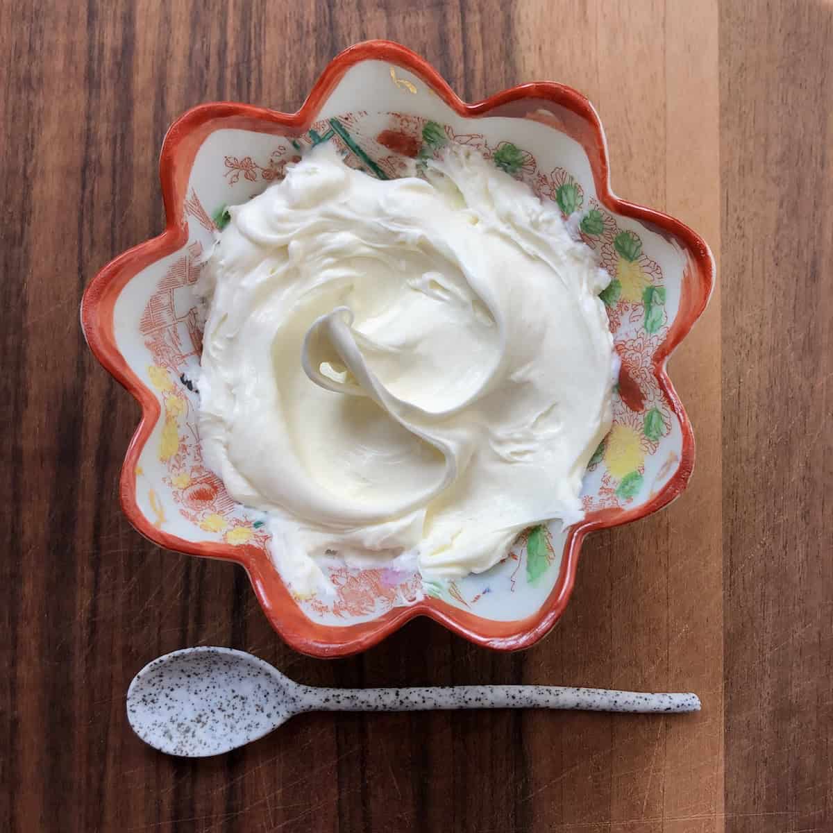 Homemade mascarpone looking luscious and creamy with a spoon in front of a small serving dish for making tiramisu.
