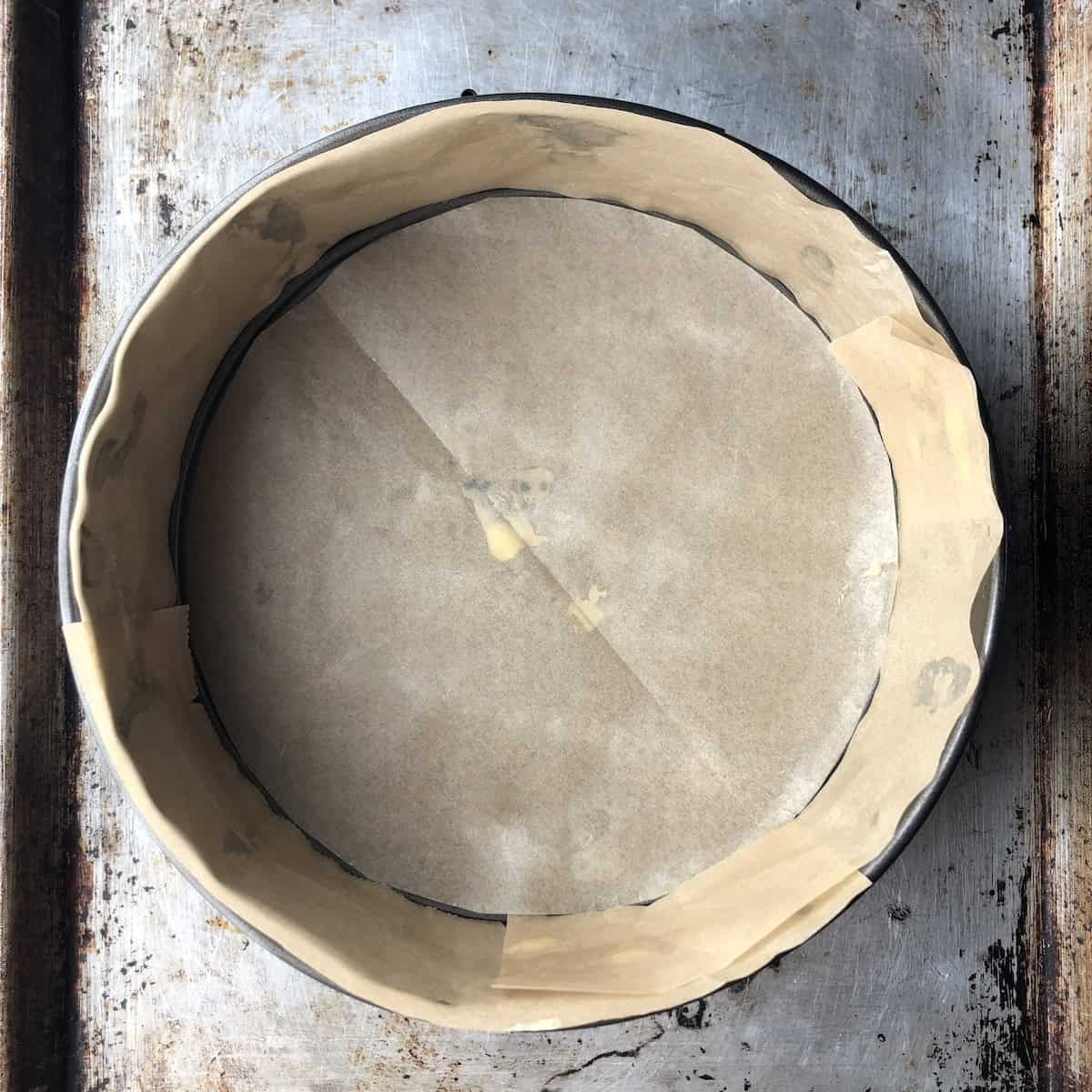 Springform pan lined with cut parchment paper round on the bottom and strips on the sides ready to layer tiramisu.
