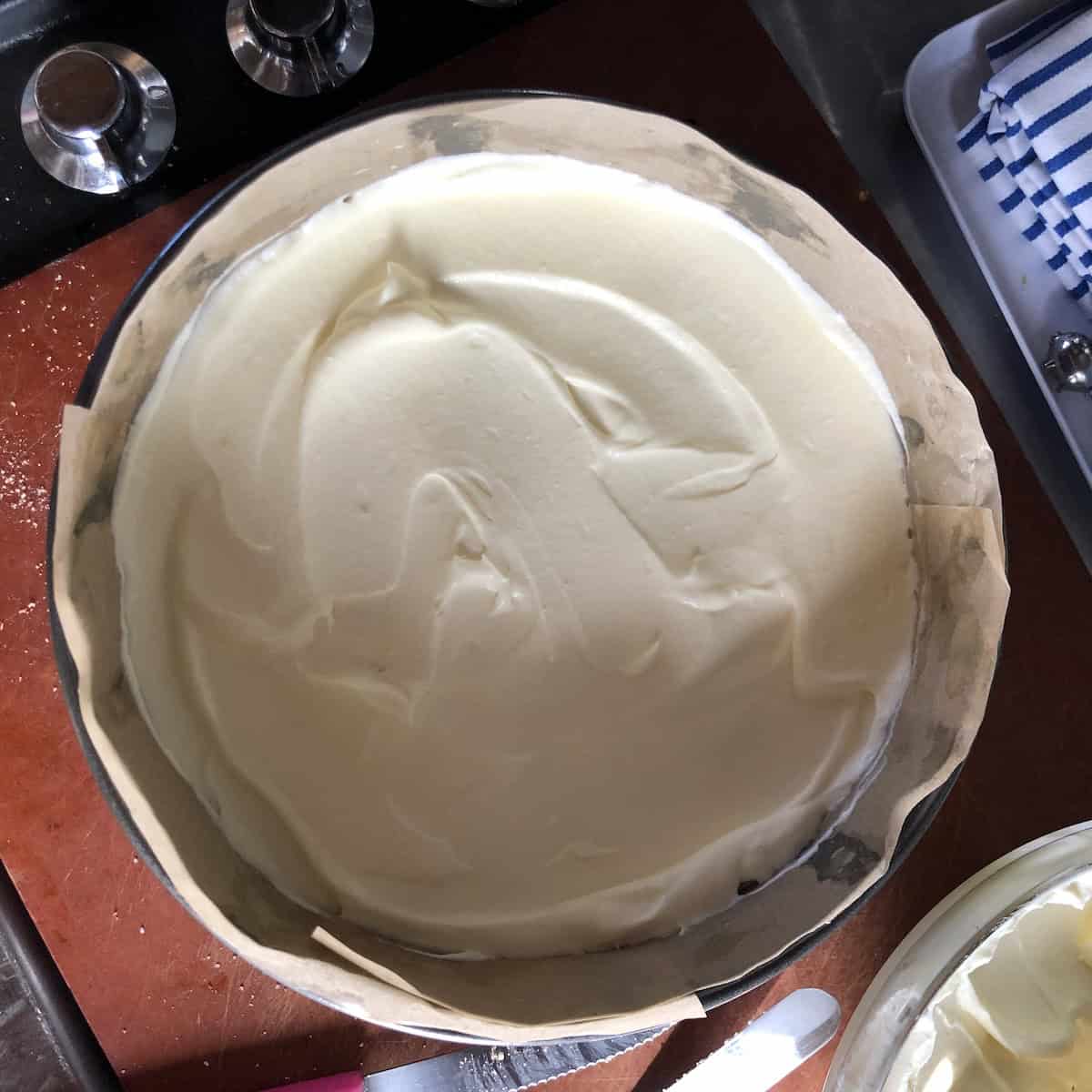 Tiramisu cream smoothed all the way to the edges of the springform pan covering the ladyfinger layer below for a clean sided tiramisu cake.