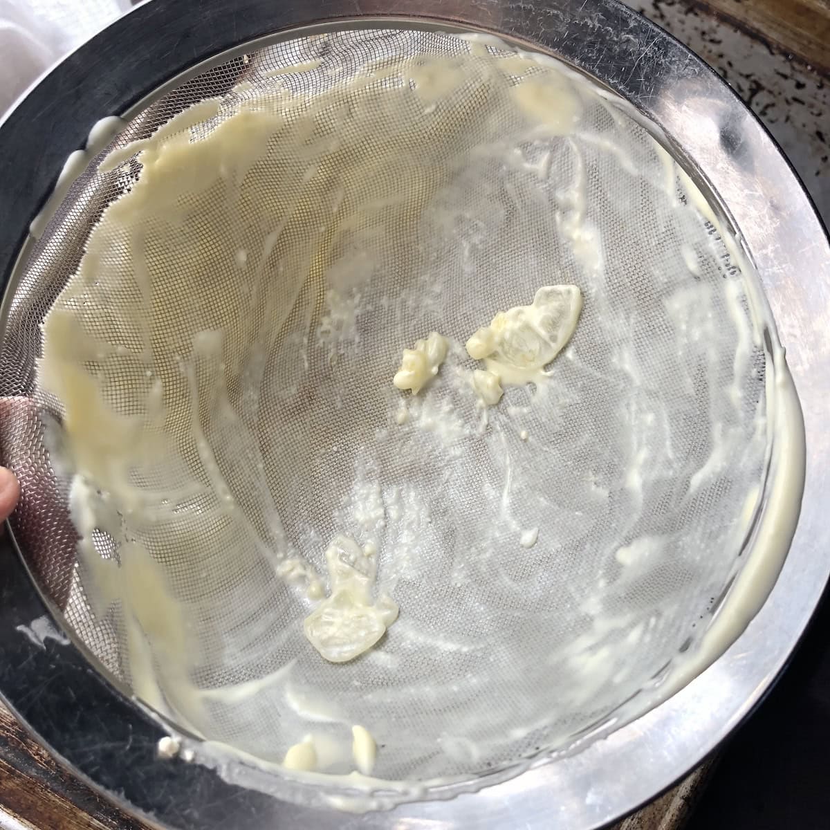 Fine mesh sieve showing the sugar shards and lumps caught after passing the tiramisu cream through for a smooth finish.