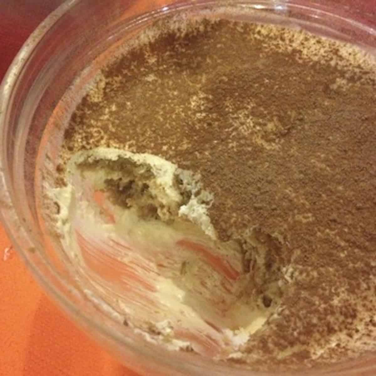 Italian restaurant tiramisu with a few bites eaten revealing the espresso soaked ladyfinger layers and mascarpone cream inside.