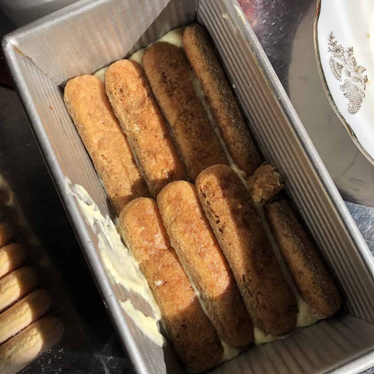 Eight inch loaf pan tiramisu with soaked ladyfingers on top of cream showing how to layer a loaf pan tiramisu, perfect size for small families to eat one and freeze one for later.