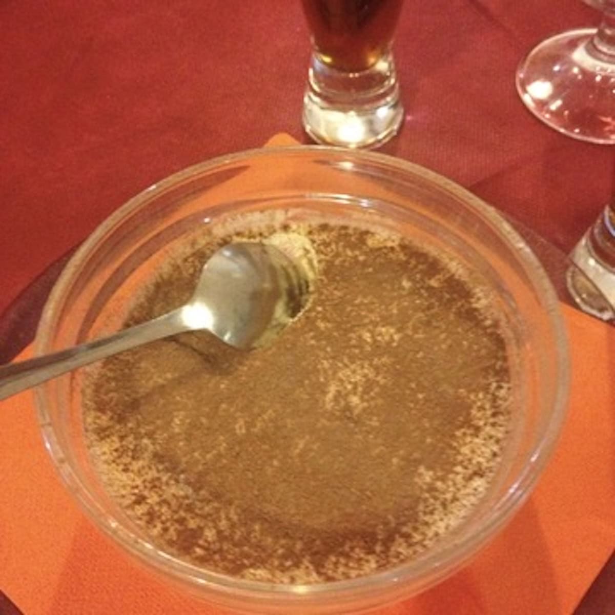 Mom and pop Italian restaurant tiramisu in a small prep bowl with cocoa powder and a spoon, individual mini serving.
