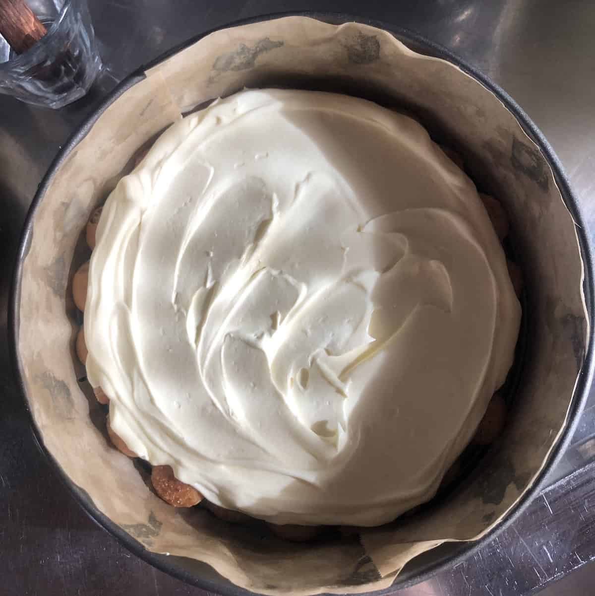 One third  of the tiramisu cream spread out evenly over the first ladyfinger layer ready for the next layer of soaked ladyfingers.