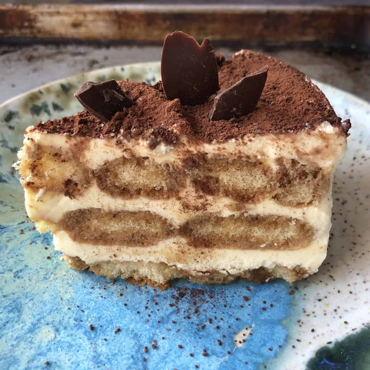 Slice cut from a mostly frozen tiramisu with perfectly clean edges, garnished with chocolate shards, cocoa powder, and uniform ladyfingers.
