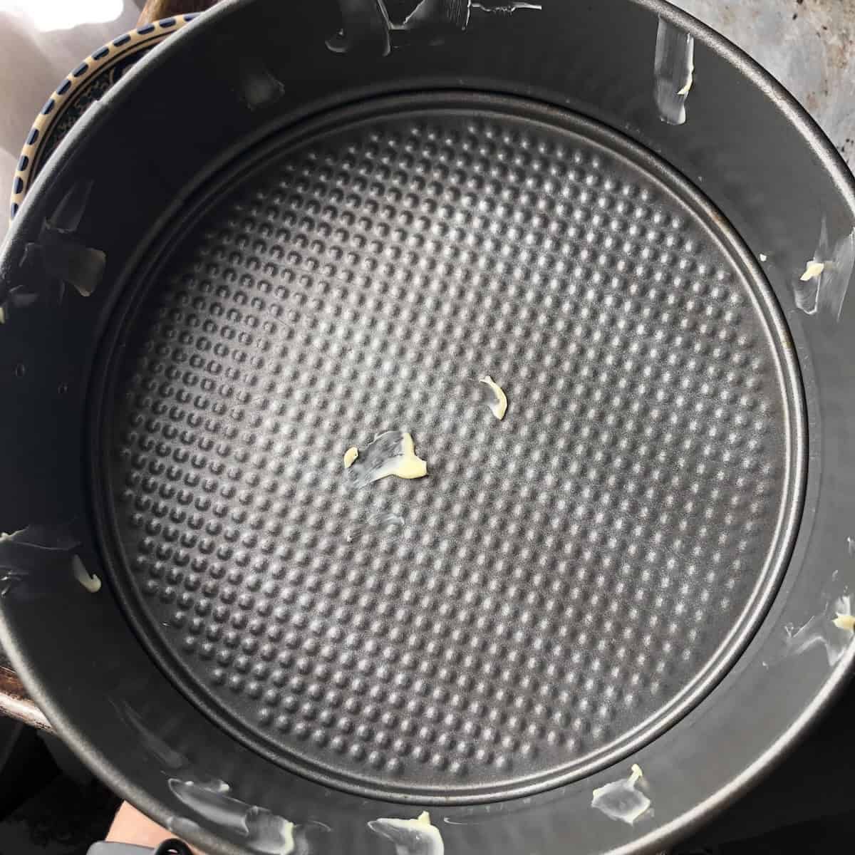 Nine inch springform pan dotted with butter on the bottom and sides to help parchment paper stick for tiramisu cake.

