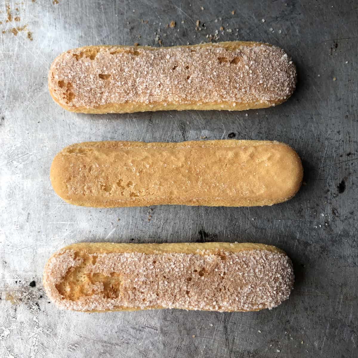 Three Vicenzi savoiardi ladyfingers on a sheet tray showing the sugar coated tops and bottom side.
