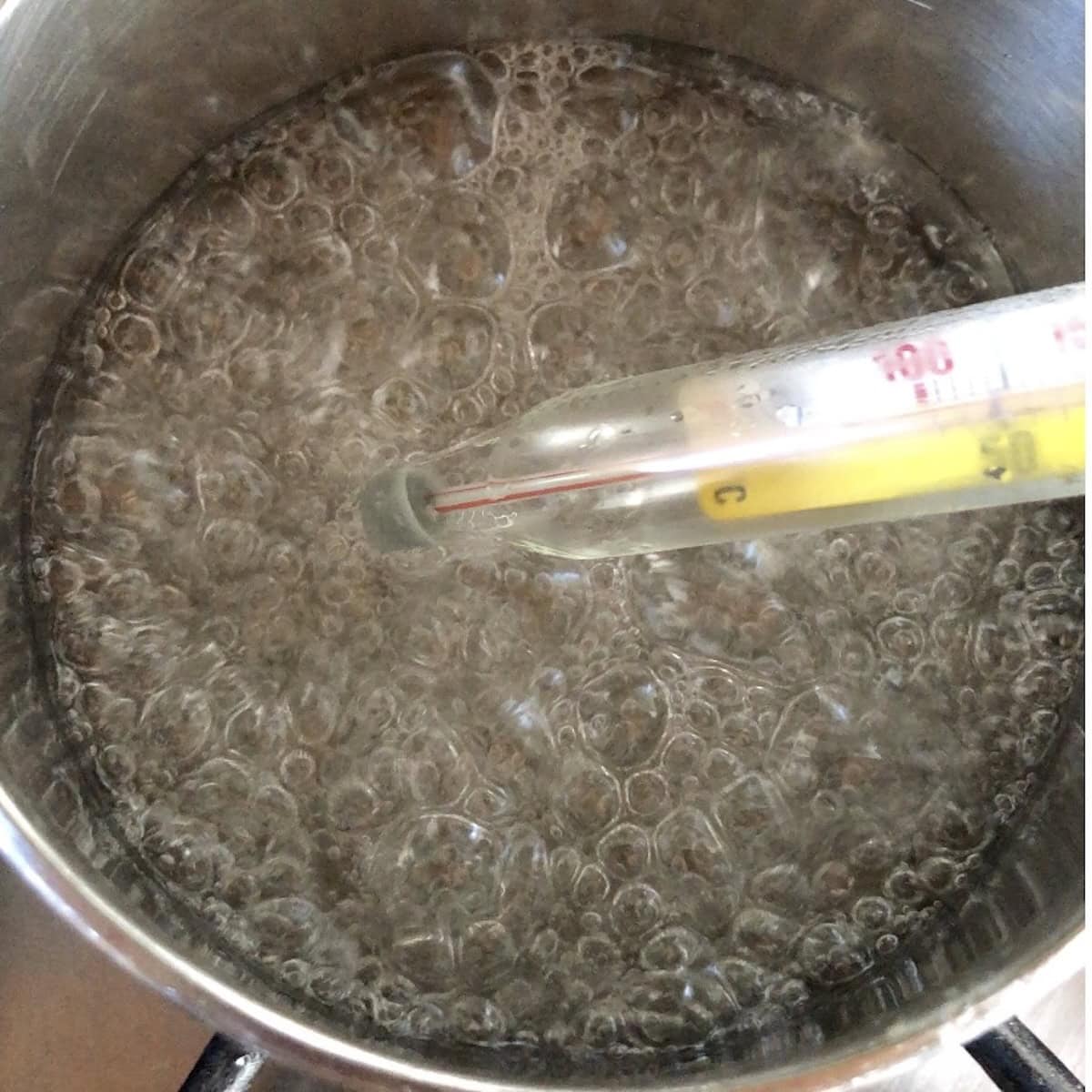 Stage three of sugar syrup with large bubbles throughout and thermometer in the middle taking the temperature for tiramisu cream.