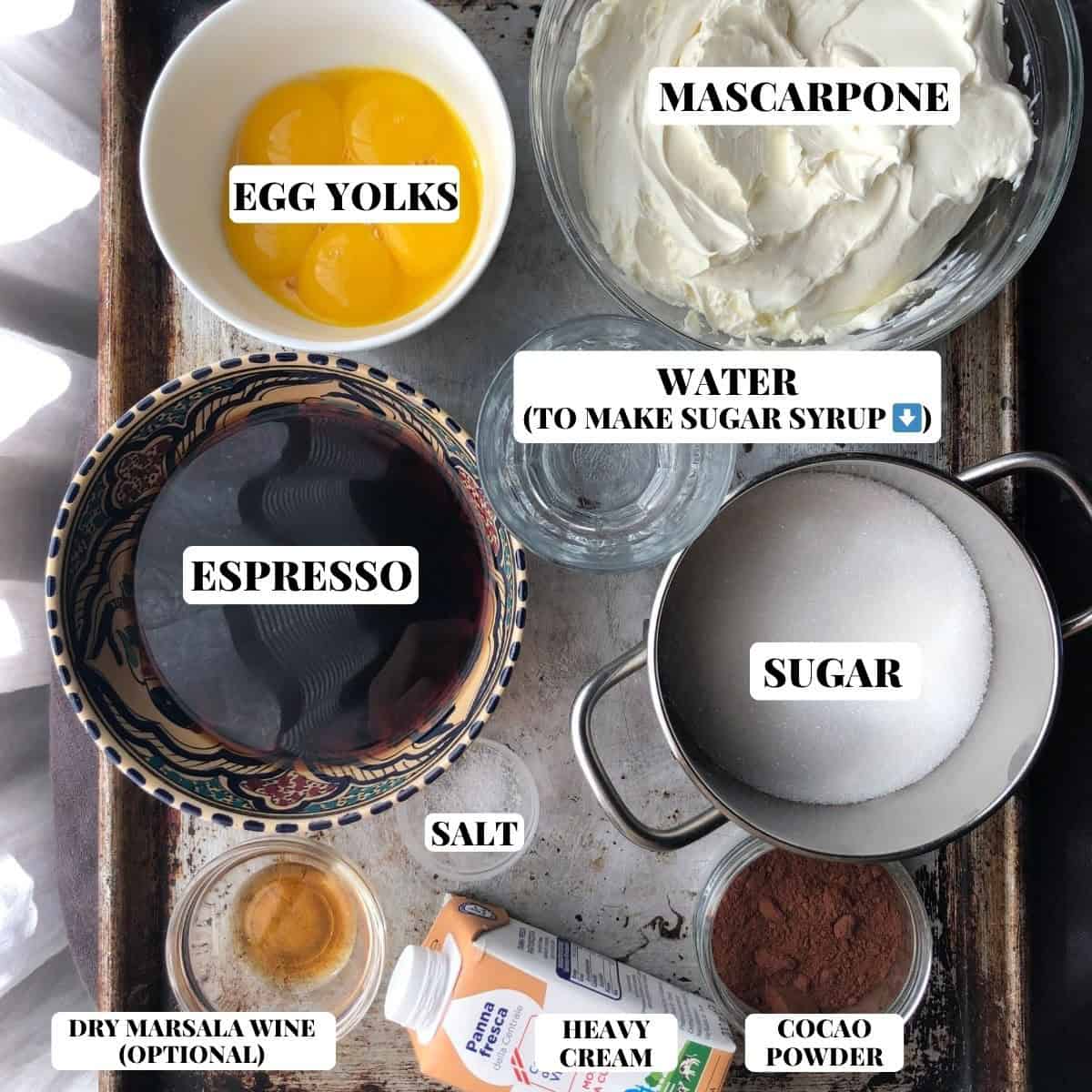 Tiramisu ingredients labeled on a sheet pan including mascarpone, ladyfingers, egg yolks, sugar, espresso, cocoa powder, salt, dry marsala, and heavy cream.