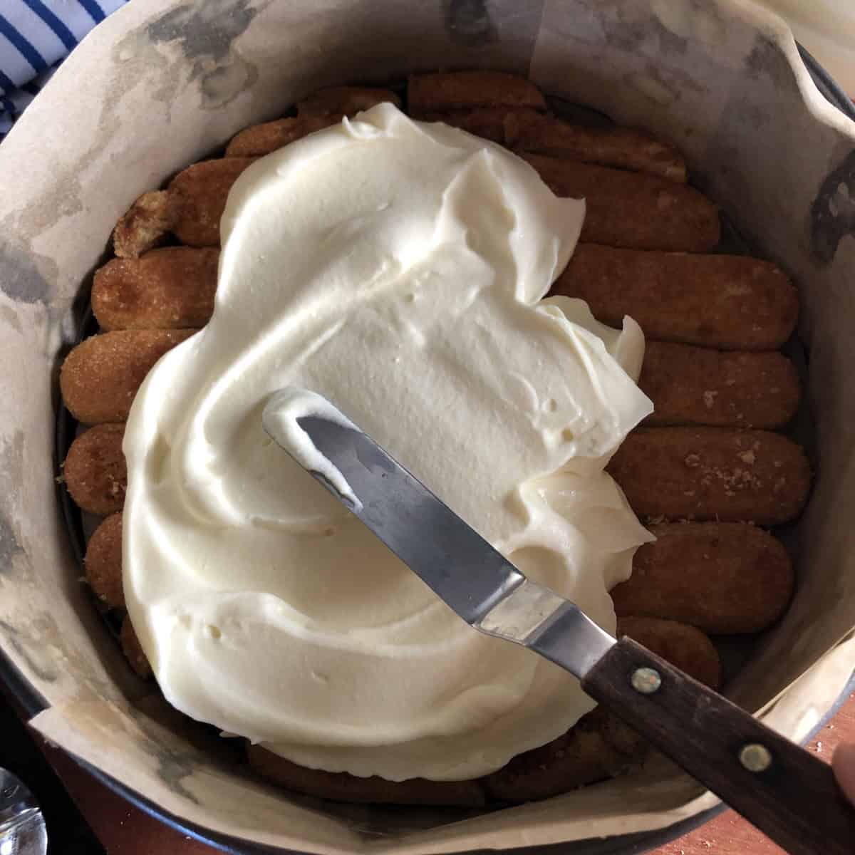 An offset spatula spreading out the mascarpone cream showing you can use this or a spoon to spread it out.
