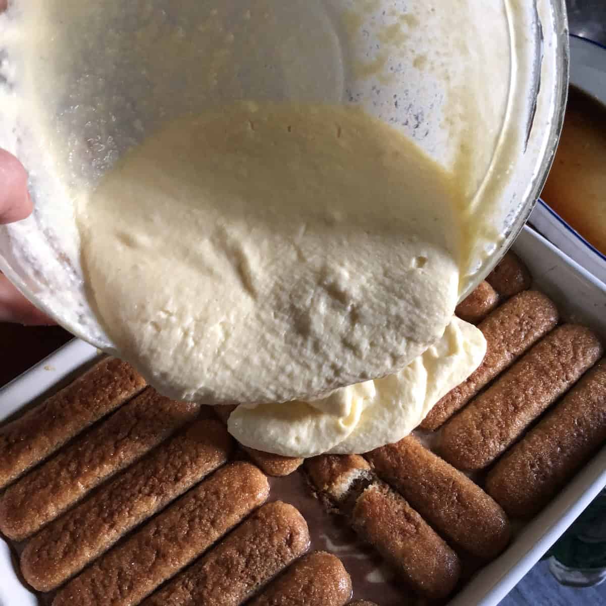 Runny tiramisu cream poured over soaked ladyfingers in a 9 by 13 casserole dish showing what failed tiramisu looks like.